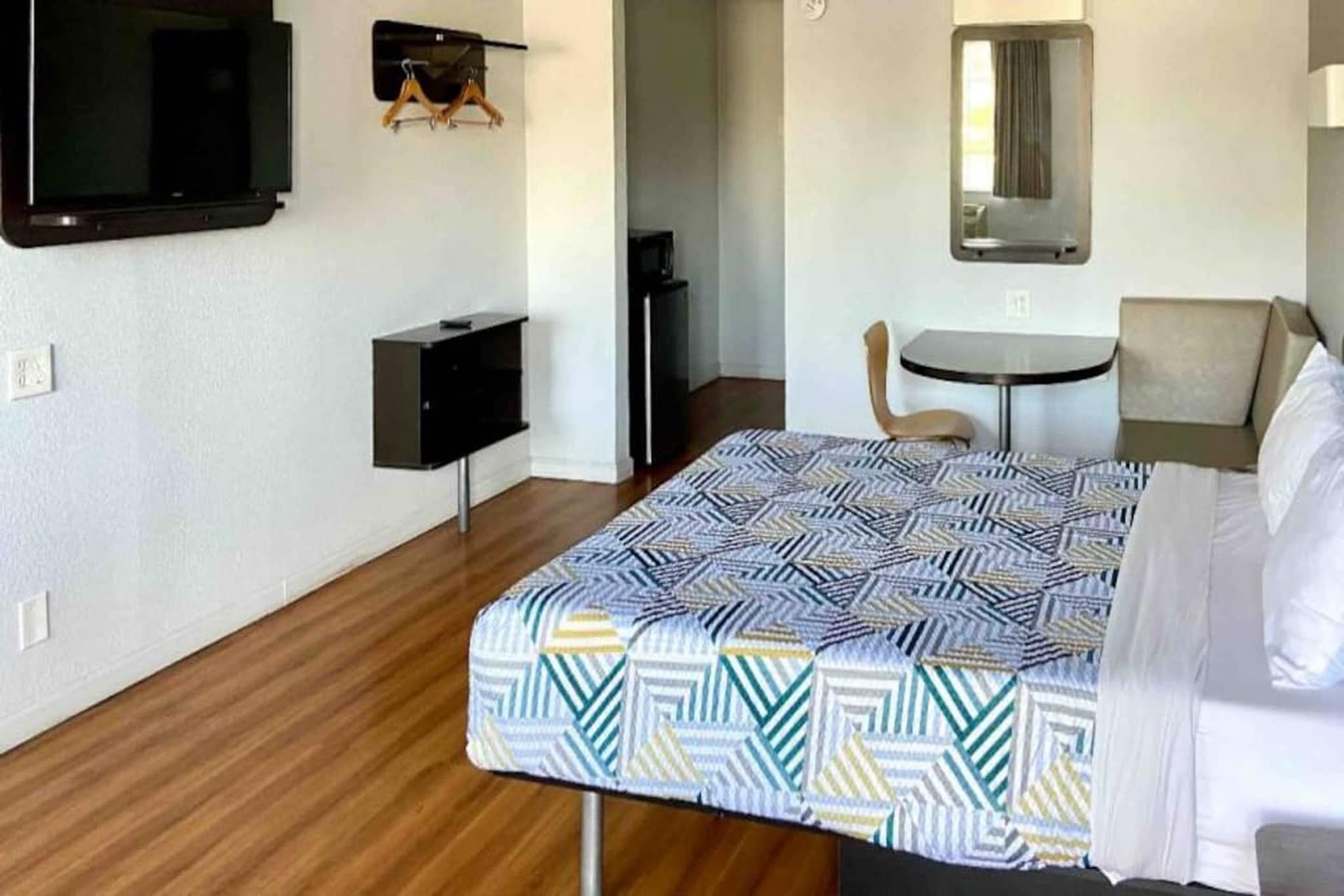 Una habitación de hotel con cama, una mesita, una silla, un televisor y un armario.