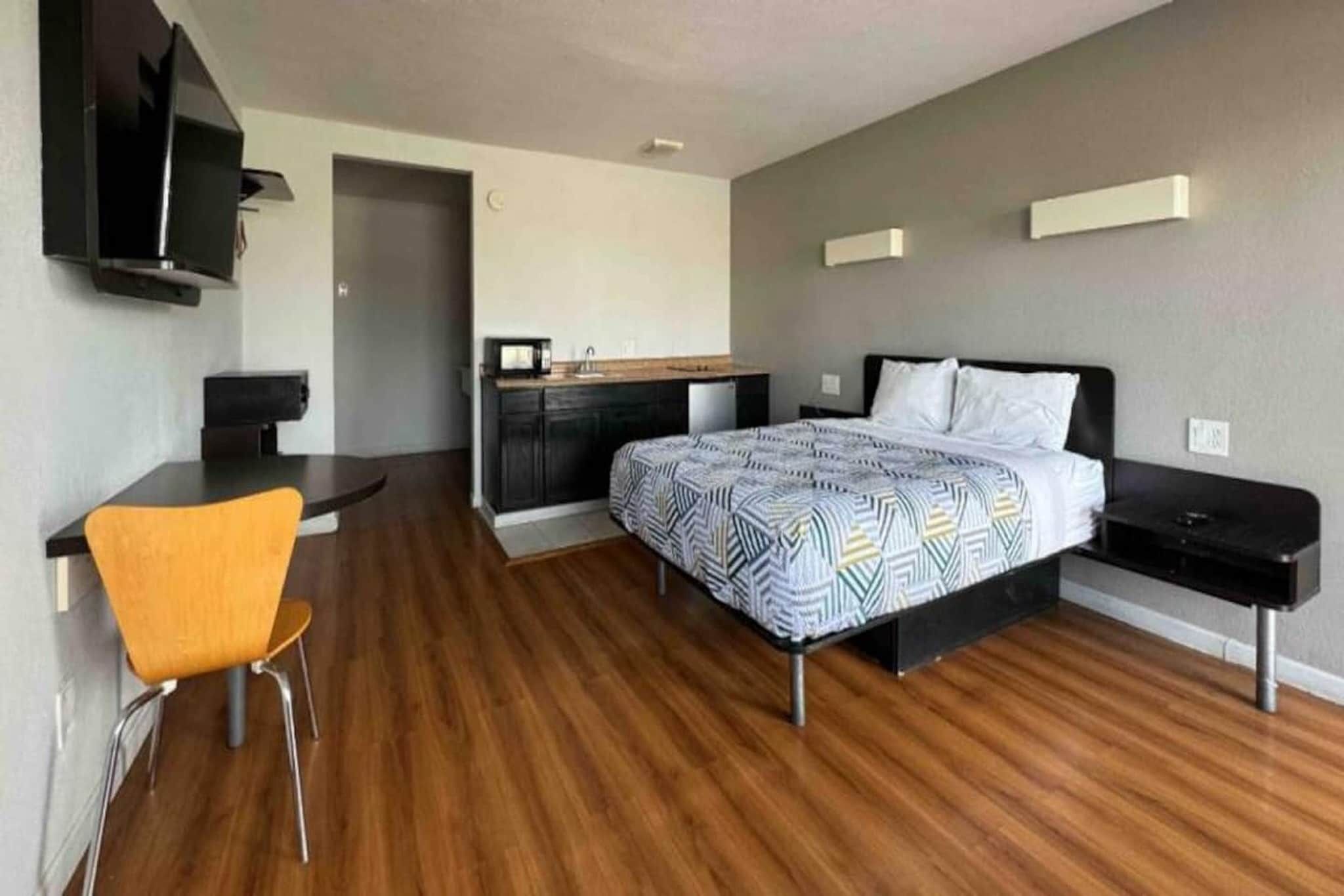 Een moderne hotelkamer met een bed, een bureau, een stoel en een kitchenette.