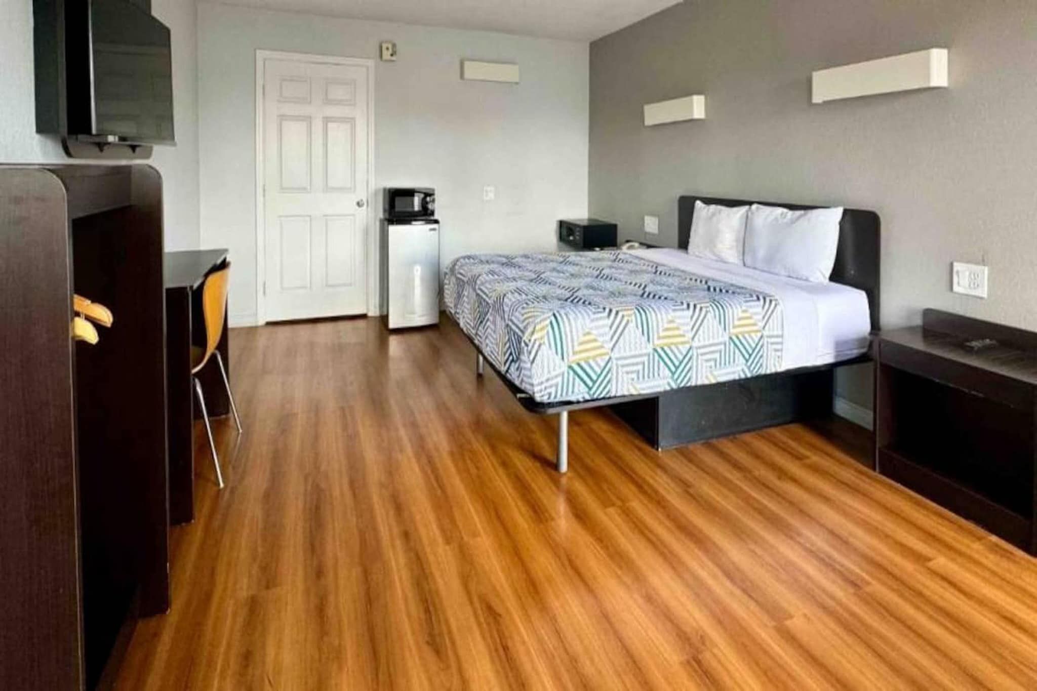 A hotel room with a bed, a desk, a chair, a wardrobe, and a television.