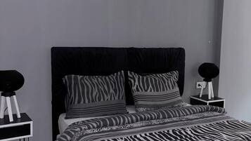 A modern bedroom with a zebra-patterned bedspread, a black headboard, and two bedside tables with round black lamps.