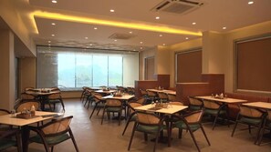 A restaurant with multiple tables and chairs, large windows, and a modern ceiling design. - HOTEL GKB MARVEL (Jaipur)