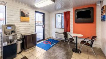 A small, modern room with a kitchenette, a seating area with a table and chairs, a television mounted on the wall, and a window with a view of the outside.