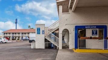 A hotel entrance with a 'Welcome' sign, a ramp for accessibility, and a parking area with cars.