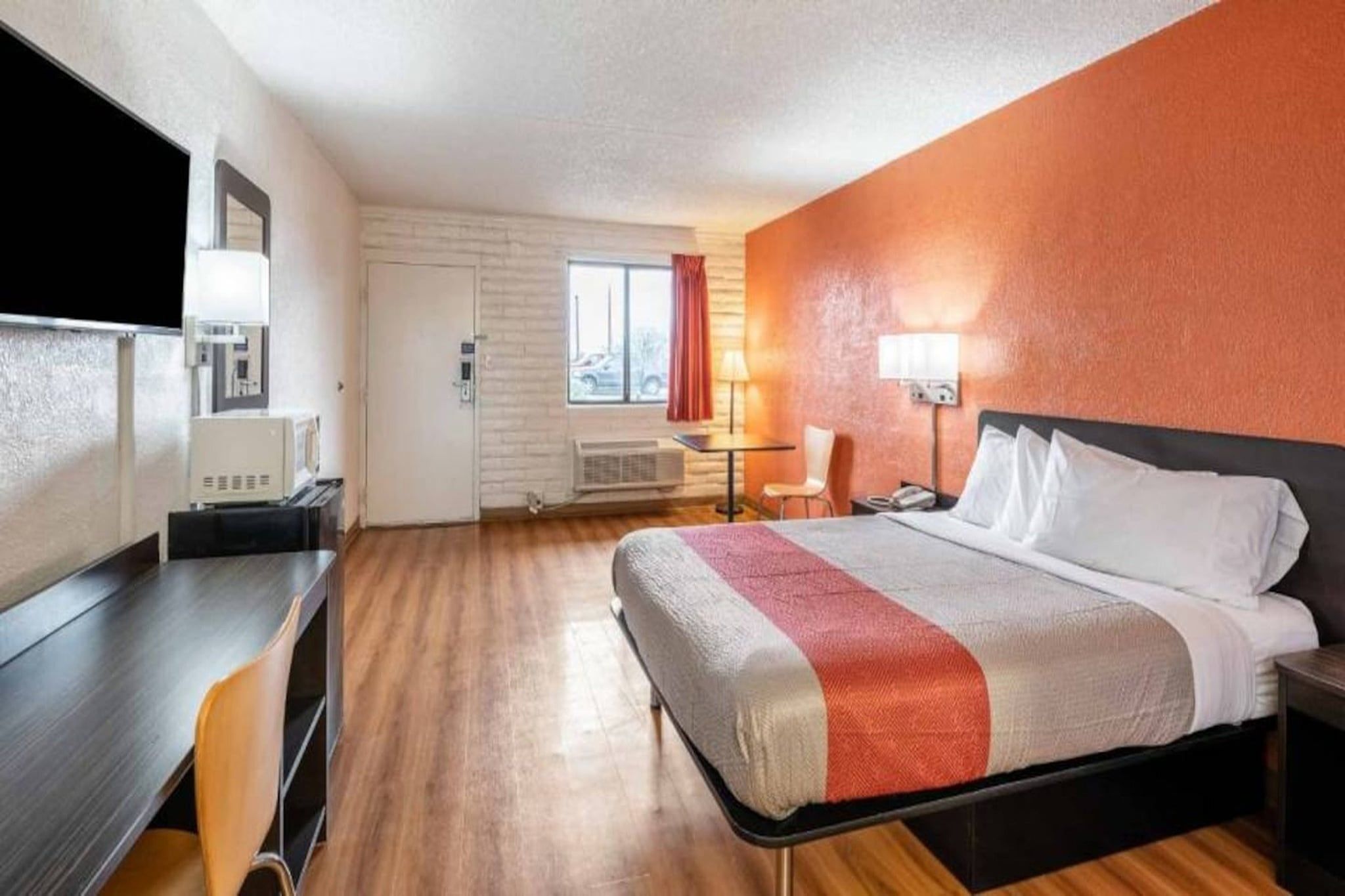 A hotel room with a bed, a desk, a chair, a lamp, and a window.
