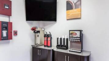 Een moderne kamer met een wandgemonteerde flatscreen televisie, een koffieapparaat, een drankdispenser en een brandmelder.