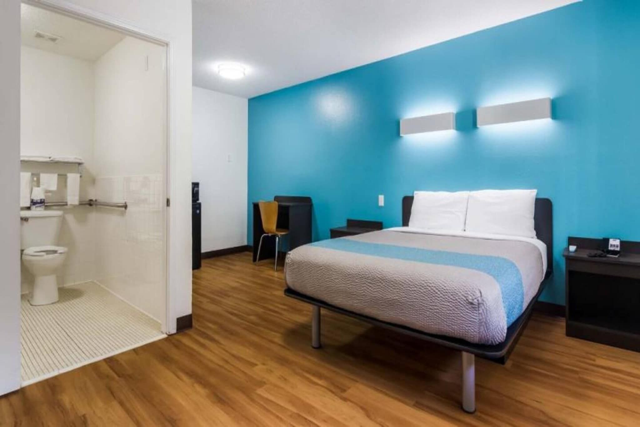 Een hotelkamer met een bed, nachtkastje, stoel, badkamer met toilet en douche.