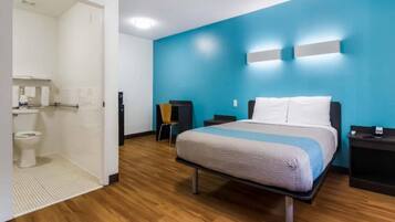 Een hotelkamer met een bed, nachtkastje, stoel, badkamer met toilet en douche.