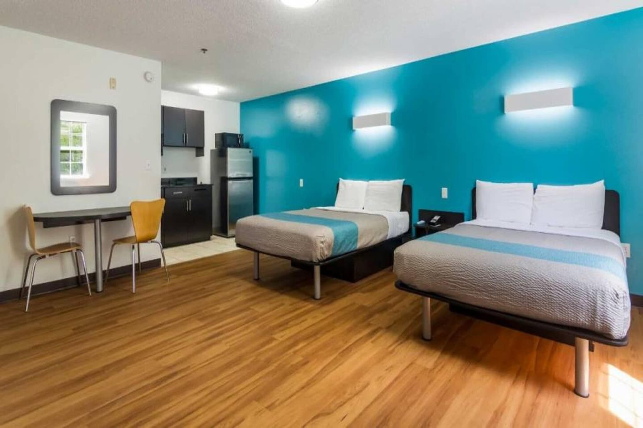 Een hotelkamer met twee bedden, een bureau, een stoel, een kitchenette en een badkamer.