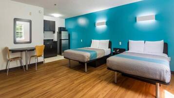 A hotel room with two beds, a desk, a chair, a kitchenette, and a bathroom.