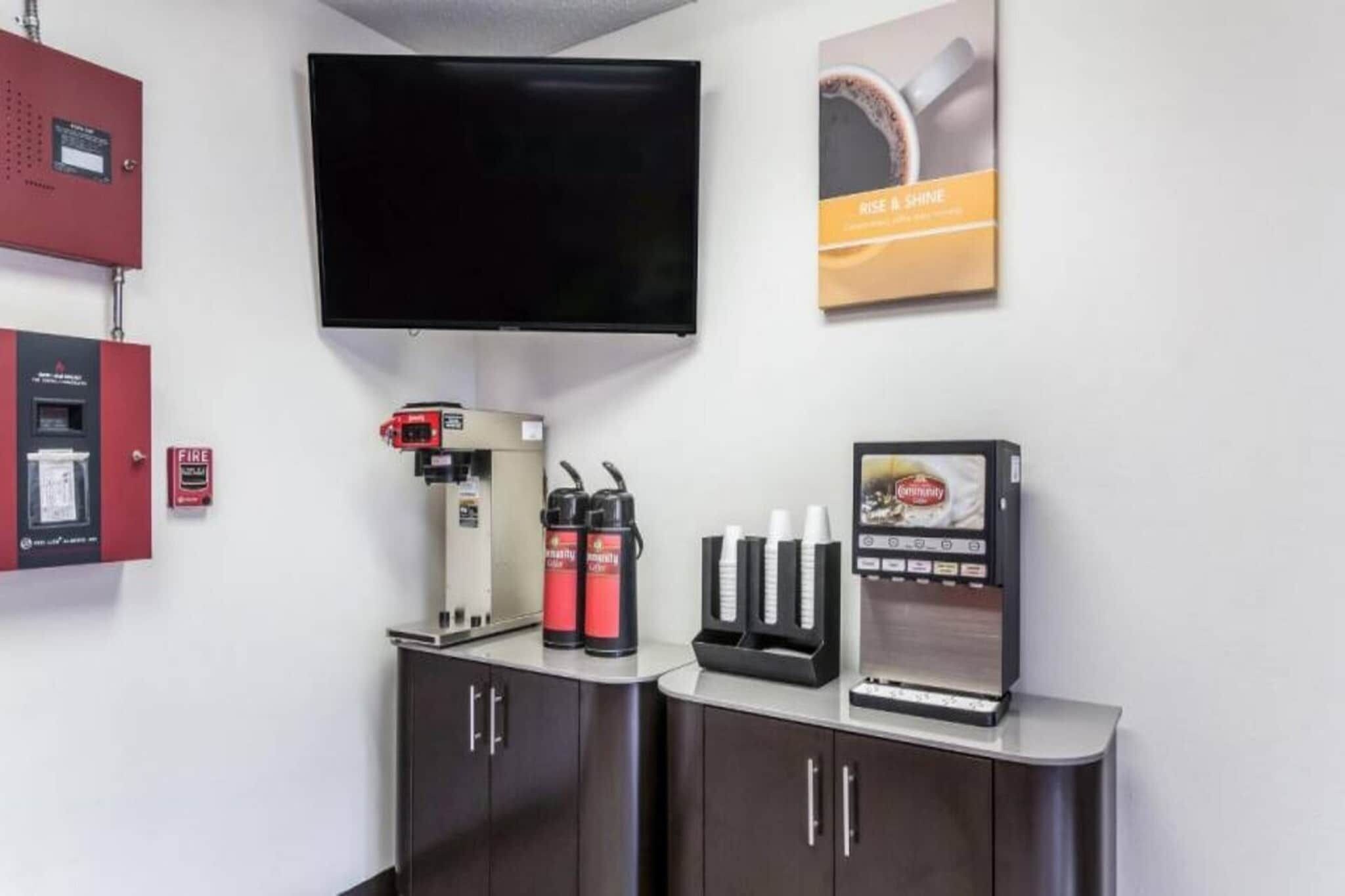 Een moderne kamer met een wandgemonteerde flatscreen televisie, een koffieapparaat, een drankdispenser en een brandmelder.