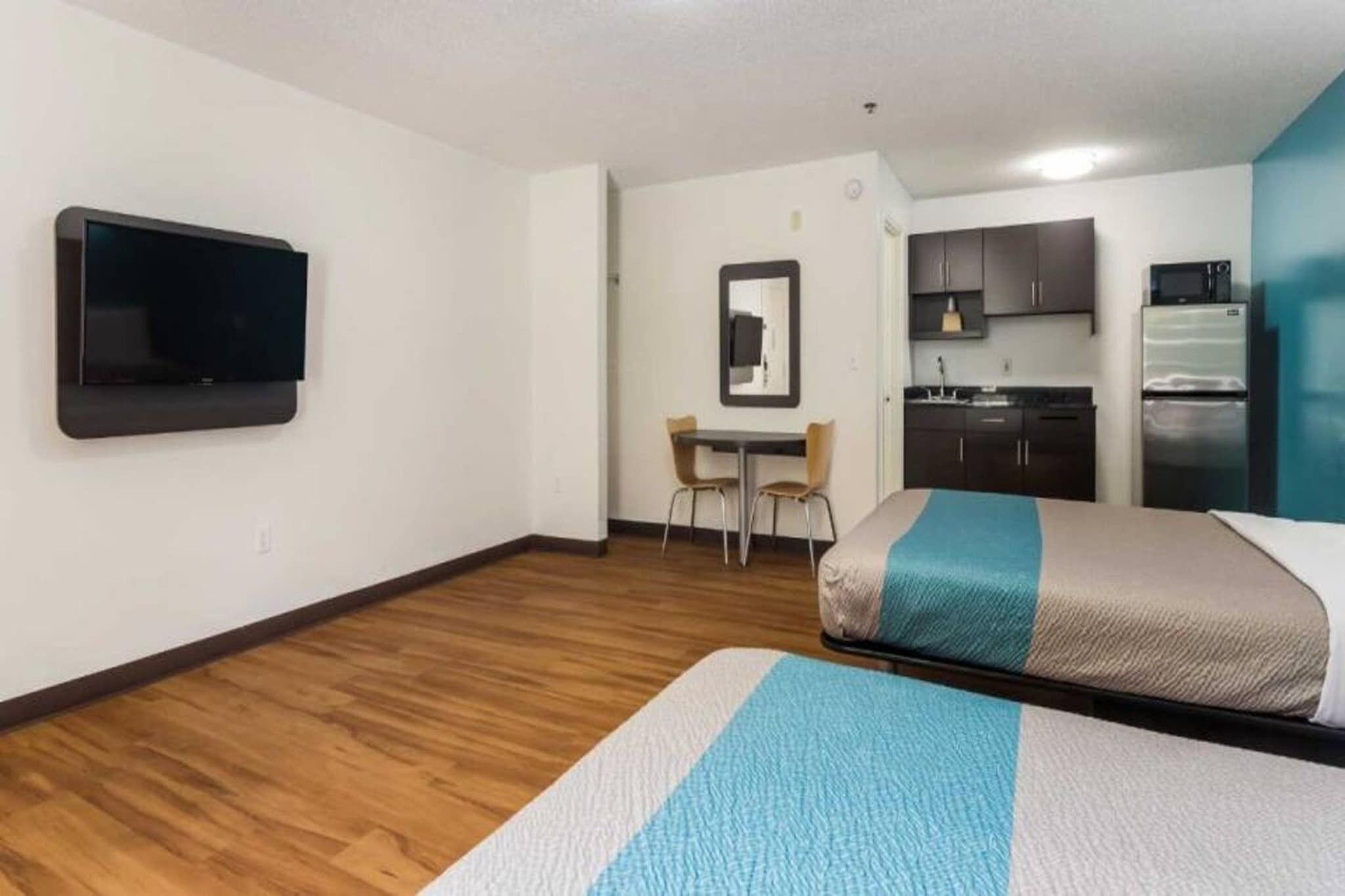 A hotel room with a bed, a desk, a chair, a television, and a kitchenette.