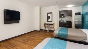 A hotel room with a bed, a desk, a chair, a television, and a kitchenette.