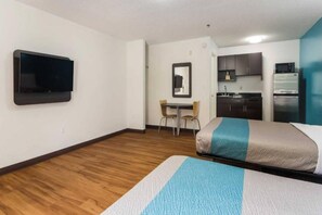 Una habitación de hotel con una cama, un escritorio, una silla, un televisor y una kitchenette.