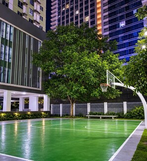 Ein Basketballplatz im Freien mit einem Baum und einem Gebäude im Hintergrund.
