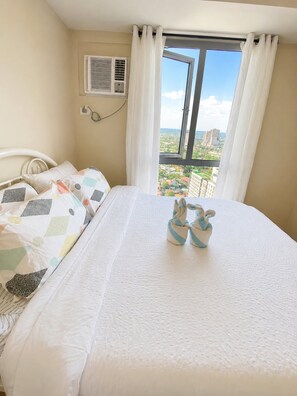 Ein Schlafzimmer mit einem Bett, Kissen, einem Fenster mit Vorhängen und einer Klimaanlage.
