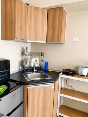 A kitchen with wooden cabinets, a black countertop, a dish rack, a sink, a stove, and a slow cooker. - Inside It park Condo unit Cebu City accessible all (Cebu City)