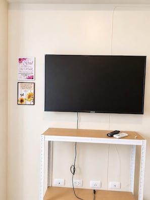 A television mounted on a wall with a wooden table below it, featuring a remote control and a power strip. - Inside It park Condo unit Cebu City accessible all (Cebu City)