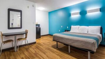 A hotel room with a bed, a desk, two chairs, a mirror, and a blue accent wall.