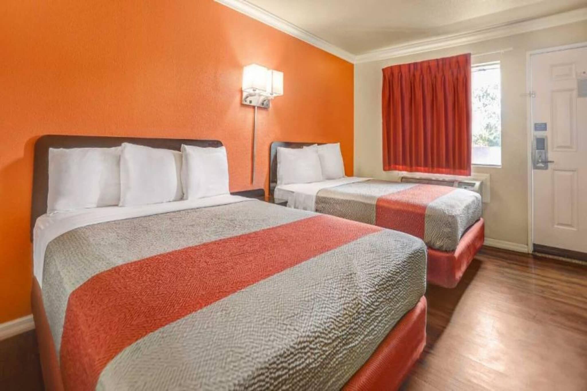 A hotel room with two beds, a window with curtains, and a door.