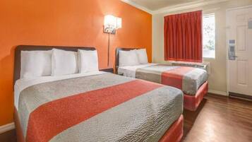 A hotel room with two beds, a window with curtains, and a door.