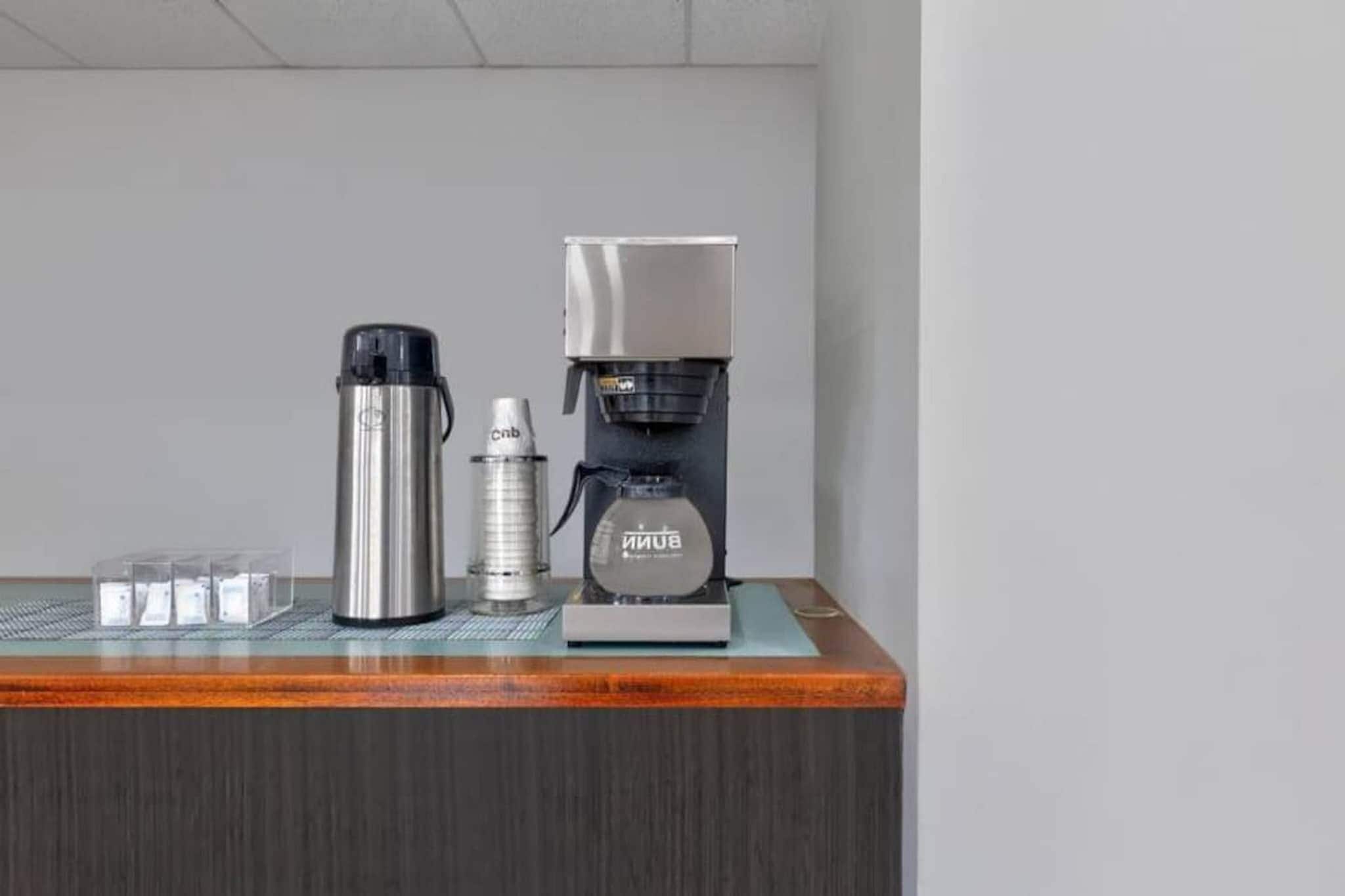 A coffee maker, a thermos, and a water bottle on a wooden counter.