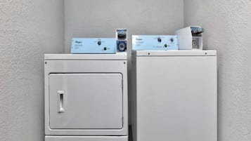 Deux appareils électroménagers blancs, probablement un lave-linge et un sèche-linge, avec des panneaux de commande situés sur le dessus, placés contre un mur à texture.