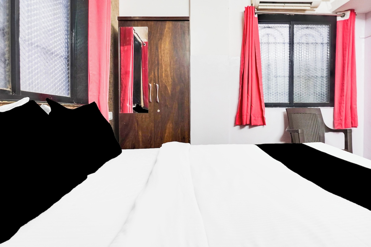 Quarto de hotel com cama, uma cadeira, guarda-roupa e janela com cortinas.