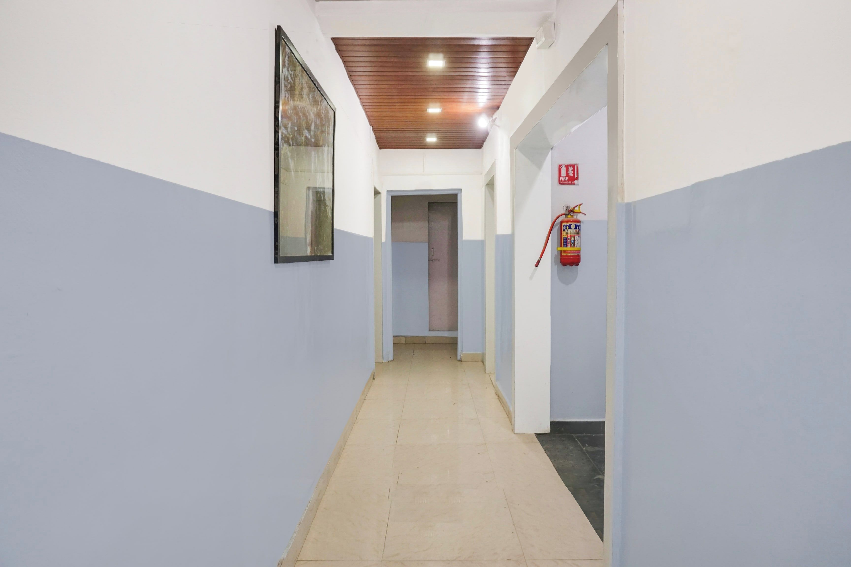 Un couloir avec un extincteur fixé au mur, une porte au fond et un plafond doté d’un éclairage encastré.
