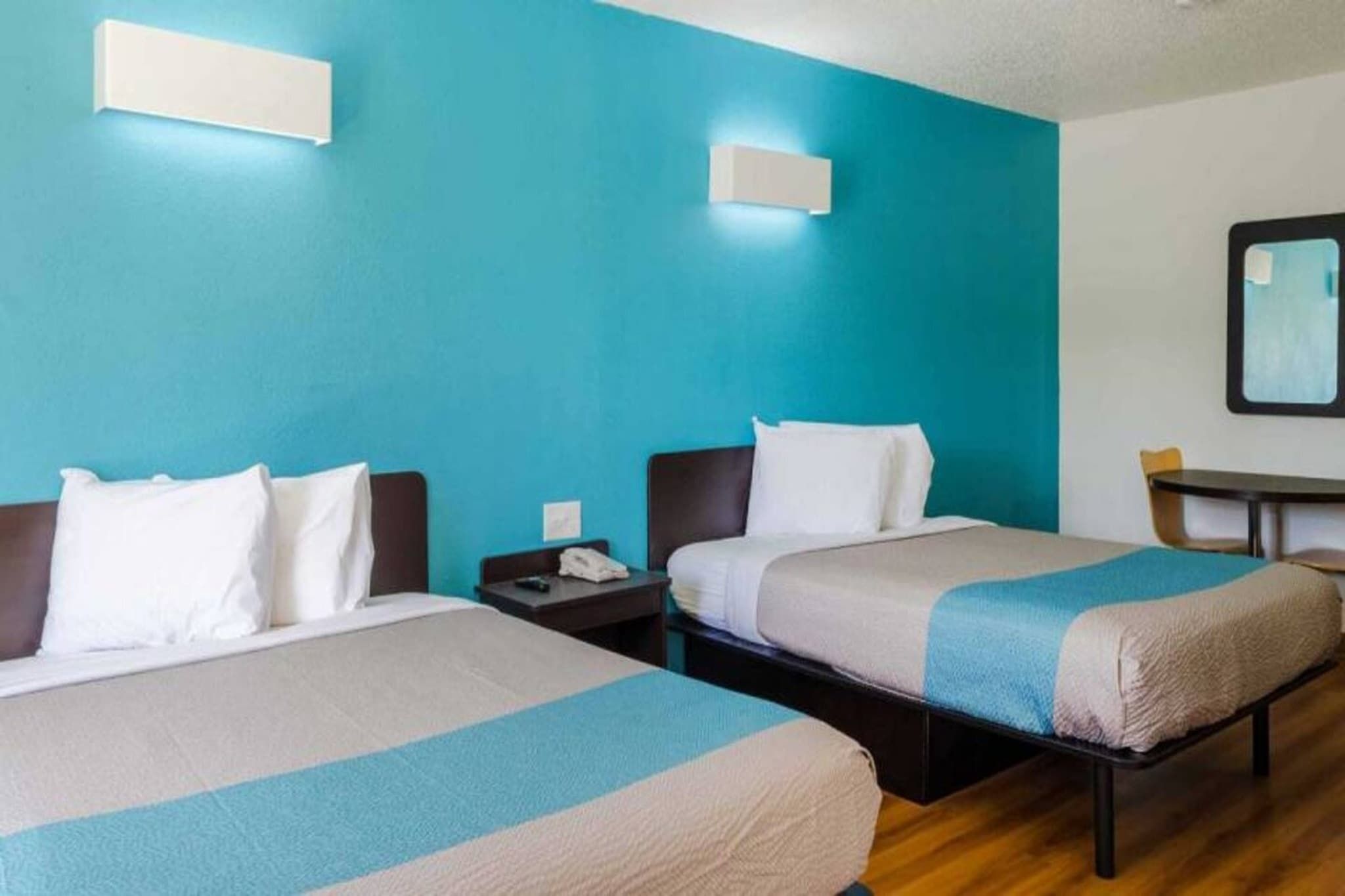 Una camera d'albergo con due letti, un comodino, una scrivania e uno specchio.