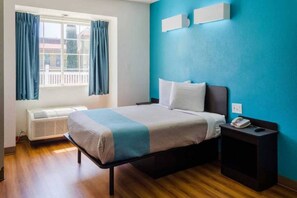 Une chambre à coucher comprenant un lit, une table de chevet, une fenêtre avec des rideaux et un luminaire fixé au mur.