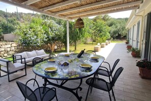 An outdoor patio with a round table set for dining, surrounded by chairs, a sofa, and a stone wall. - Capovillas - Country Villa Armonia with privat pool (zambrone)