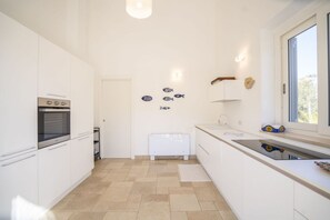 A modern kitchen with white cabinets, a built-in oven, and a window with a view. - Capovillas - Country Villa Armonia with privat pool (zambrone)