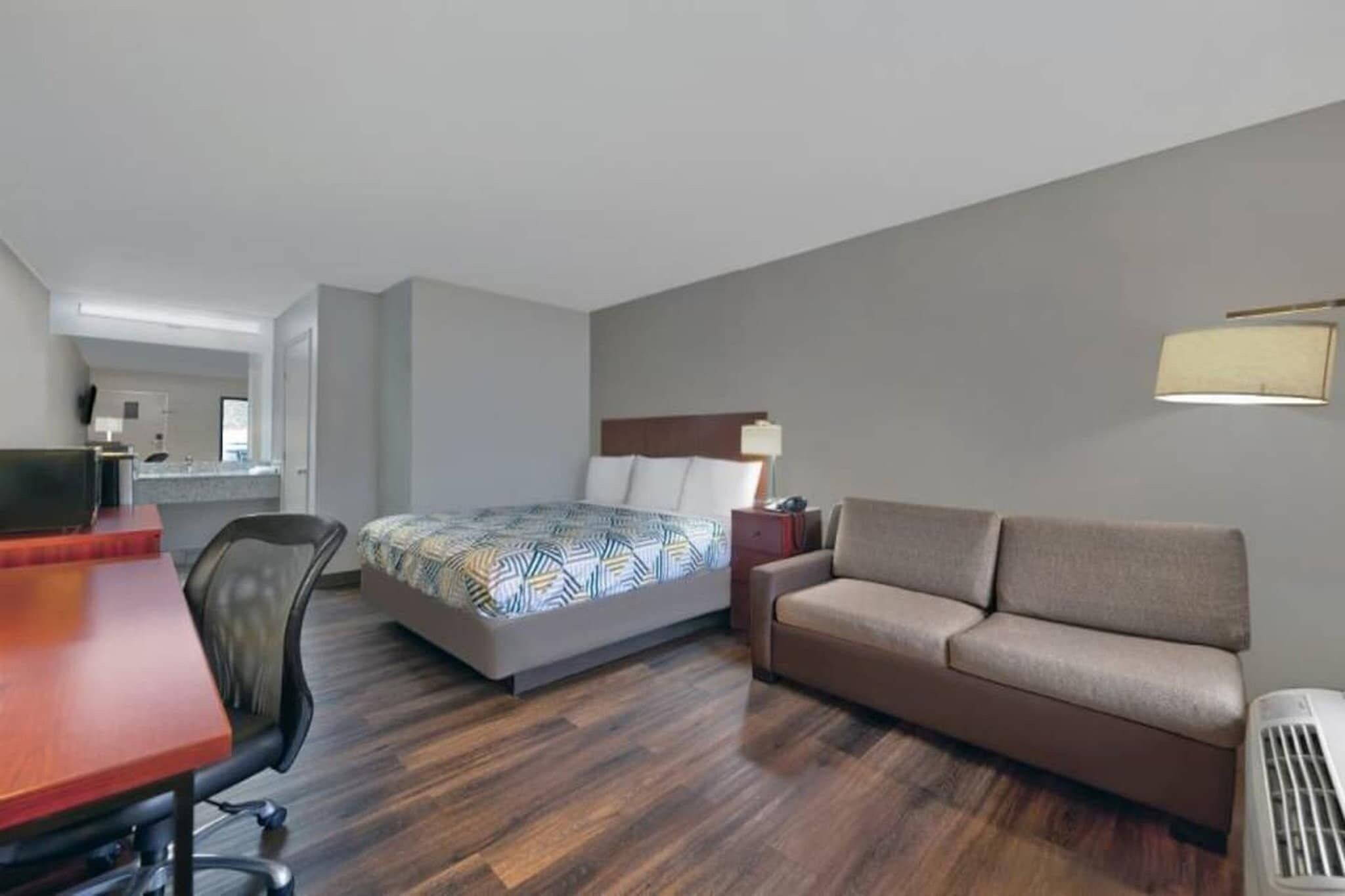 A hotel room with a bed, a sofa, a desk, and a chair.