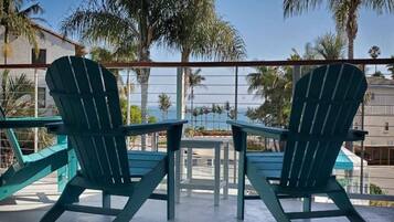 Duas cadeiras Adirondack de frente para uma mesa em uma varanda, com vista para palmeiras e um prédio ao fundo.