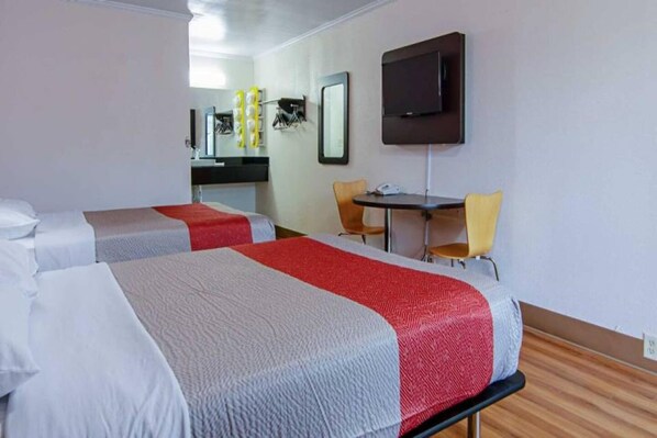 A hotel room with two beds, a desk, a chair, and a television.