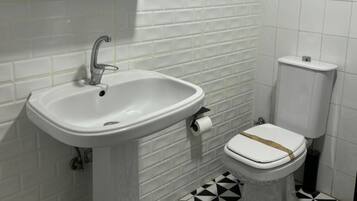 Un baño con lavamanos blanco, inodoro y suelo de baldosas.