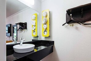 A modern bathroom with a round sink, a mirror, and a yellow towel dispenser.