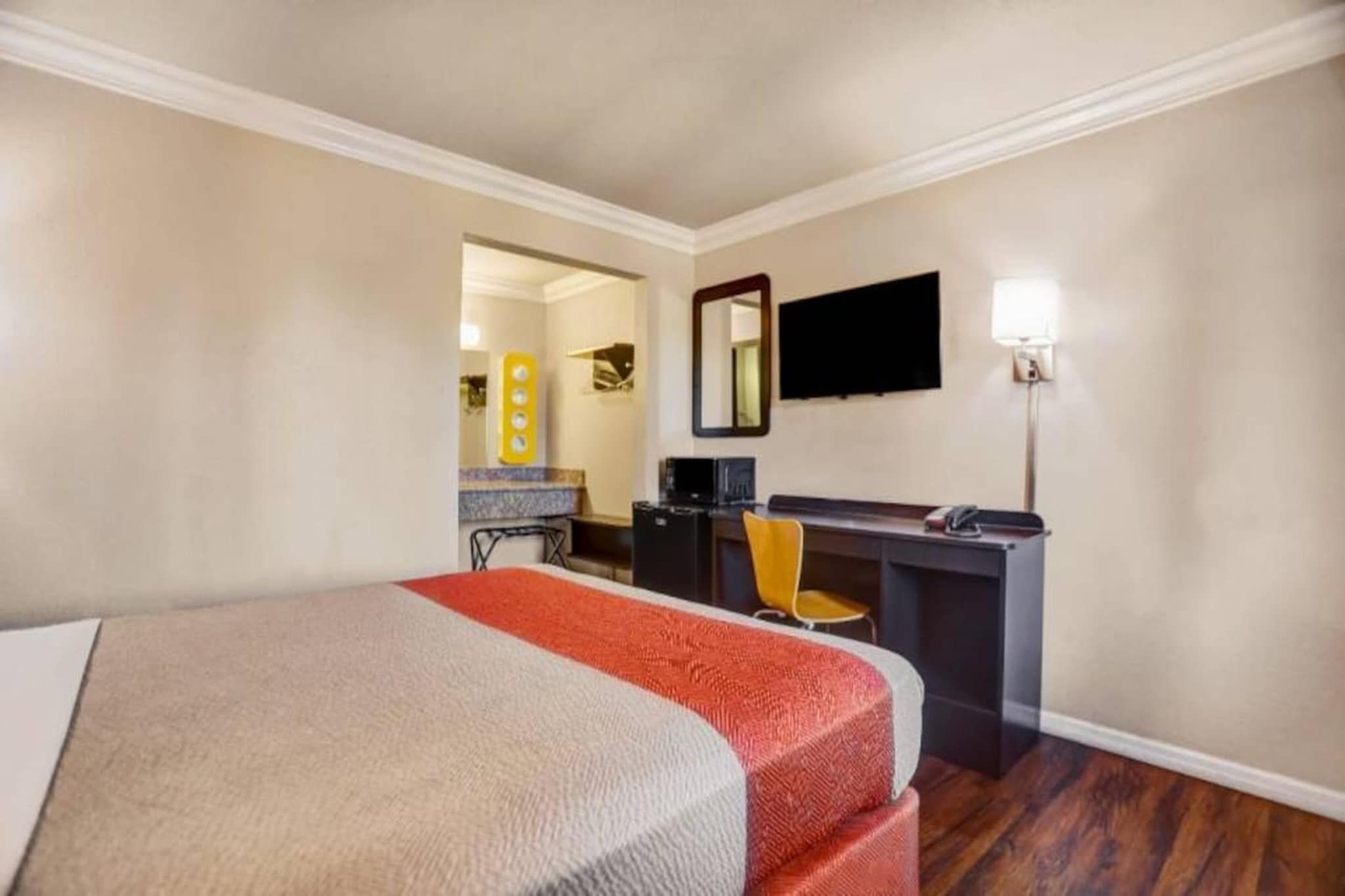 A hotel room with a bed, a desk, a chair, a television, and a mirror.