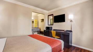 A hotel room with a bed, a desk, a chair, a television, and a mirror.