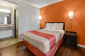 A hotel room with a bed, a nightstand, a mirror, and a bathroom visible in the background.