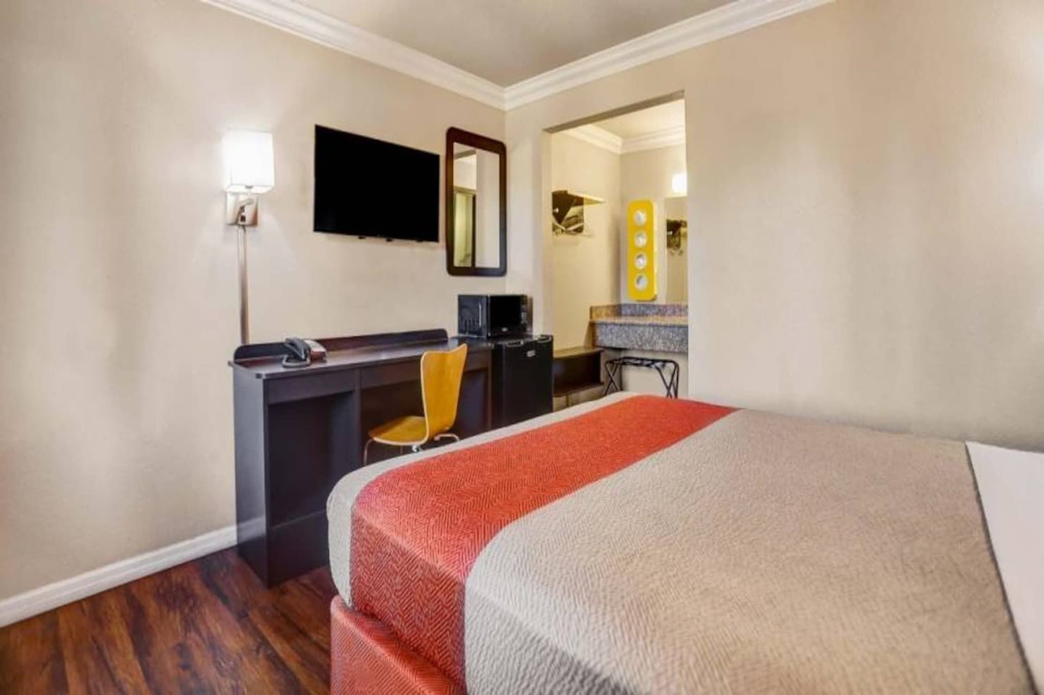 Una habitación de hotel con una cama, un escritorio, una silla, un televisor y un espejo.