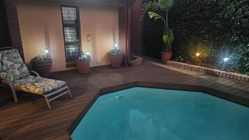 A pool area with a wooden deck, a lounge chair, and potted plants.