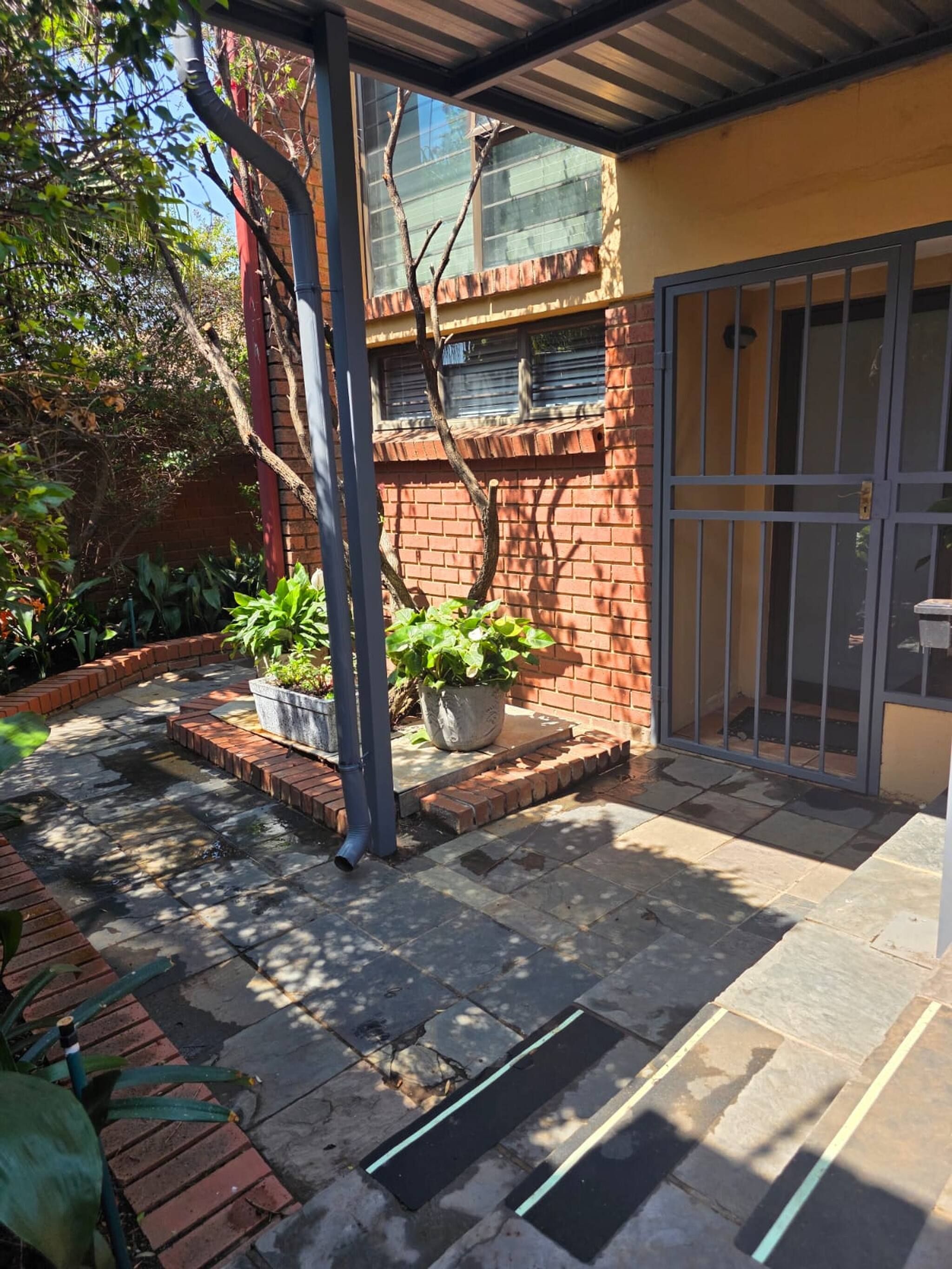 A courtyard with a brick wall, potted plants, a metal gate, and a tiled floor.