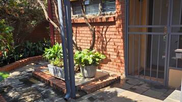 A courtyard with a brick wall, potted plants, a metal gate, and a tiled floor.