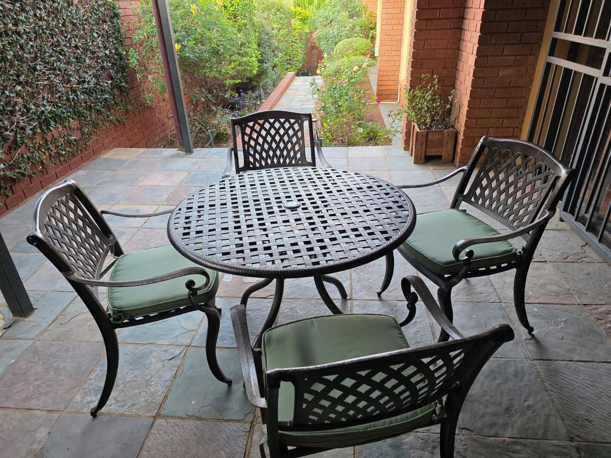 A patio with a round table and four chairs, surrounded by a brick wall and greenery.
