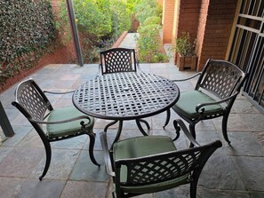 A patio with a round table and four chairs, surrounded by a brick wall and greenery. - On the Ridge Apartment (Pretoria)