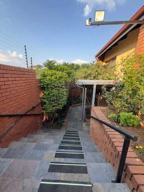 A staircase leading to a covered outdoor area with a brick wall on one side and a garden on the other. - On the Ridge Apartment (Pretoria)