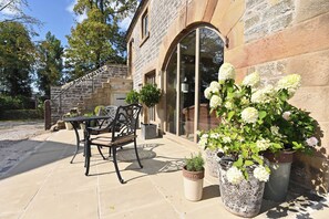 A stone building with a patio area featuring outdoor furniture and potted plants. - Butterton Barn (Leek)