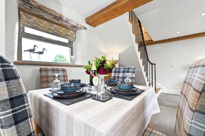 A dining area with a table set for four, featuring blue and brown dinnerware, a bottle of champagne, and a vase with flowers. - Butterton Barn (Leek)