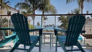 Two Adirondack chairs facing each other with a view of palm trees and a building in the background.